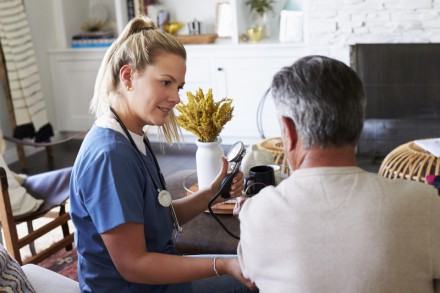 Back view of female healthcare worker measuring the blood pressure of senior man during a home visit