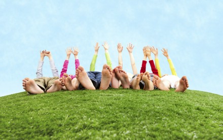 Image of several children lying on the grass and stretching their hands to the sun